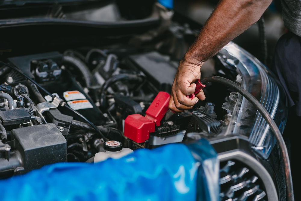 Maintenance de Batterie de Voiture et Câbles de Démarrage Un mécanicien branche des câbles de démarrage sur la batterie d'une voiture avec des bornes rouges protectrices.