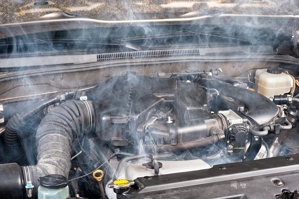 Moteur qui fume : que faire en cas de surchauffe moteur ? Moteur de voiture en surchauffe dégageant une épaisse fumée blanche sous le capot ouvert.