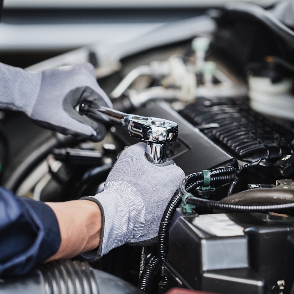 Réparation Moteur Voiture : Maintenance et Mécanique Mains d'un mécanicien avec gants gris utilisant une clé à cliquet pour réparer un moteur de voiture.